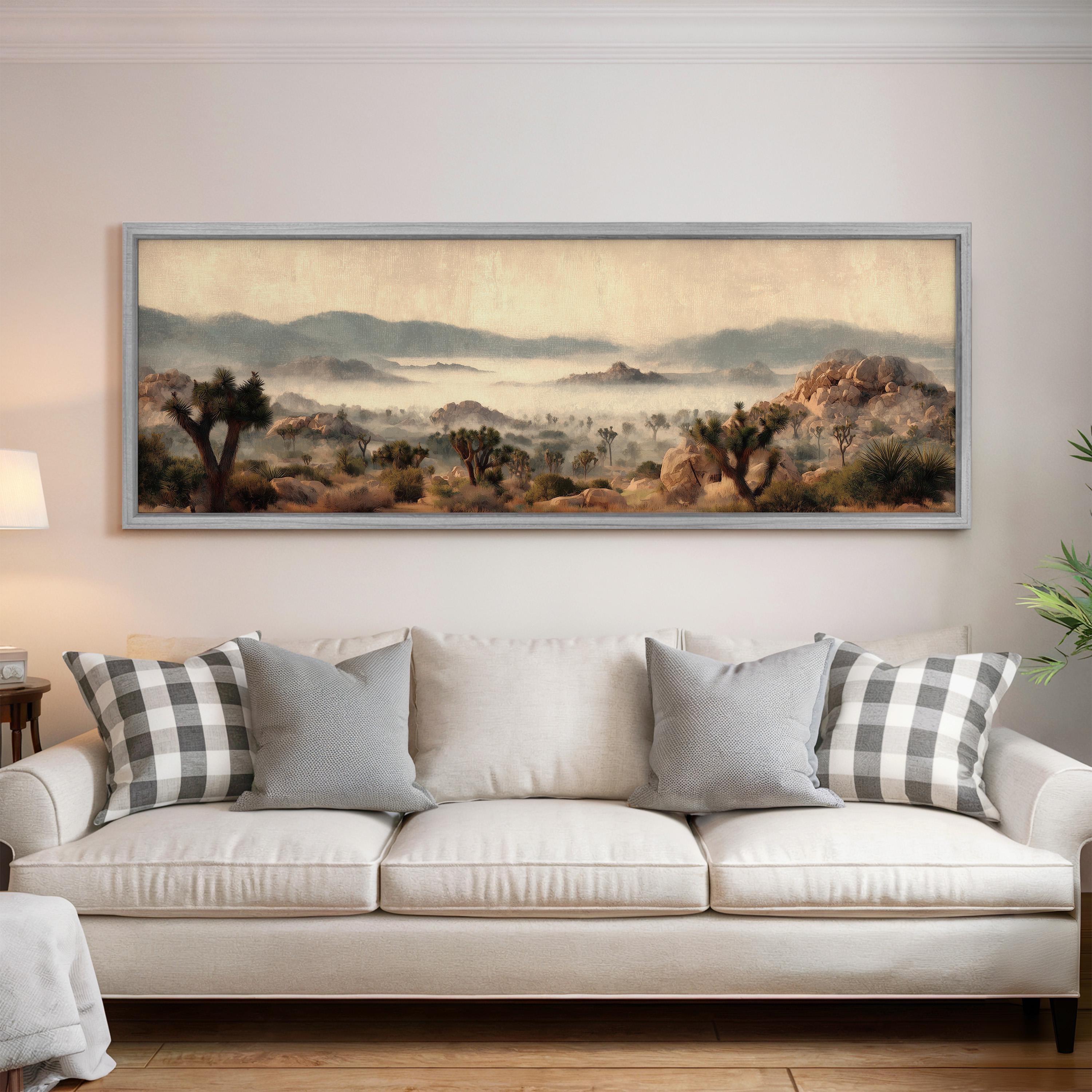 a large landscape painting hanging on a wall above a white sofa with gray and white plaid throw pillows.