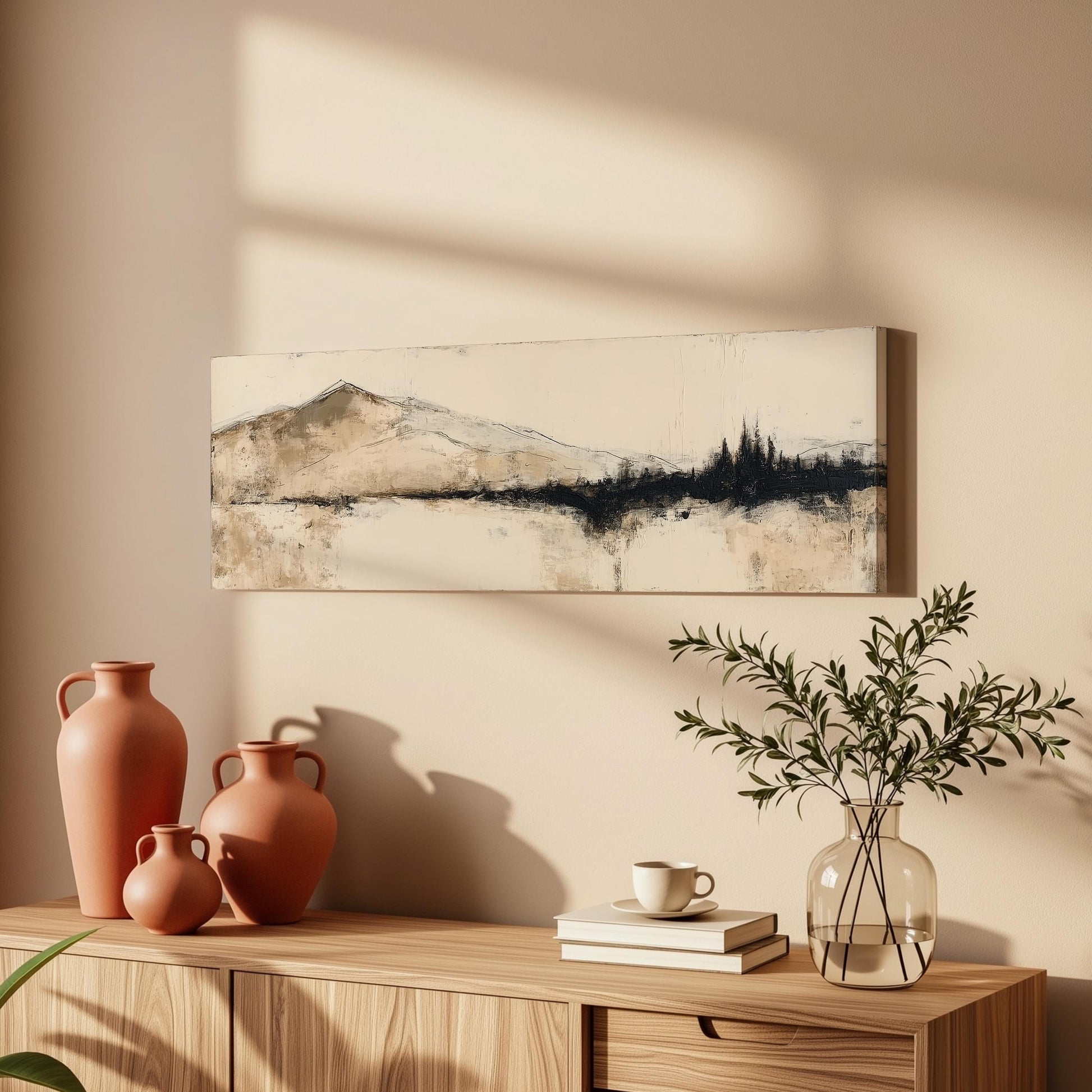 a wooden cabinet with a painting of a mountain landscape hanging on the wall above it. The cabinet also has three orange vases and a glass vase with greenery, as well as a stack of books and a coffee cup on the surface.