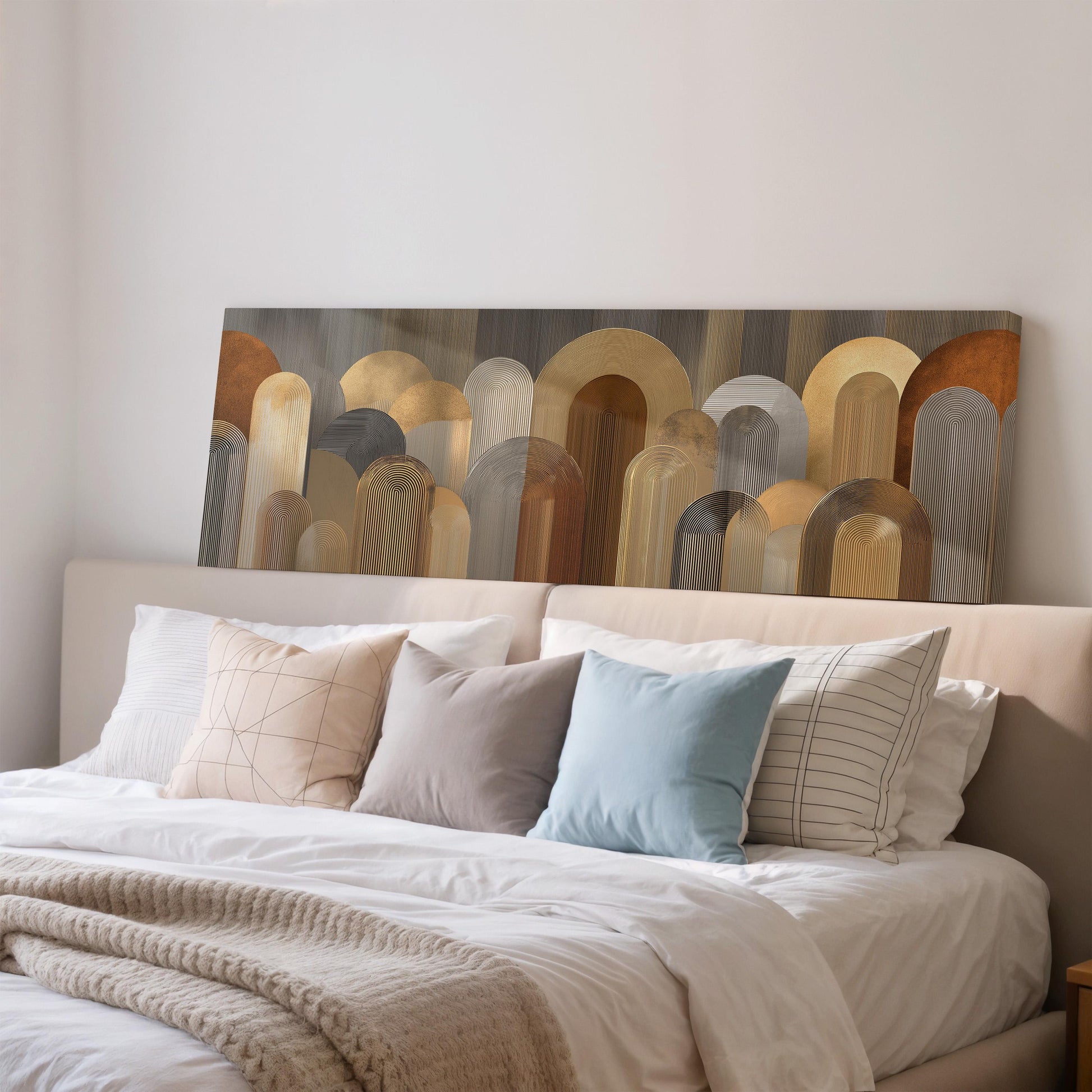 a large bed with a white comforter and a variety of pillows in different colors and patterns. The bed is set against a wall with a large abstract painting hanging above it.