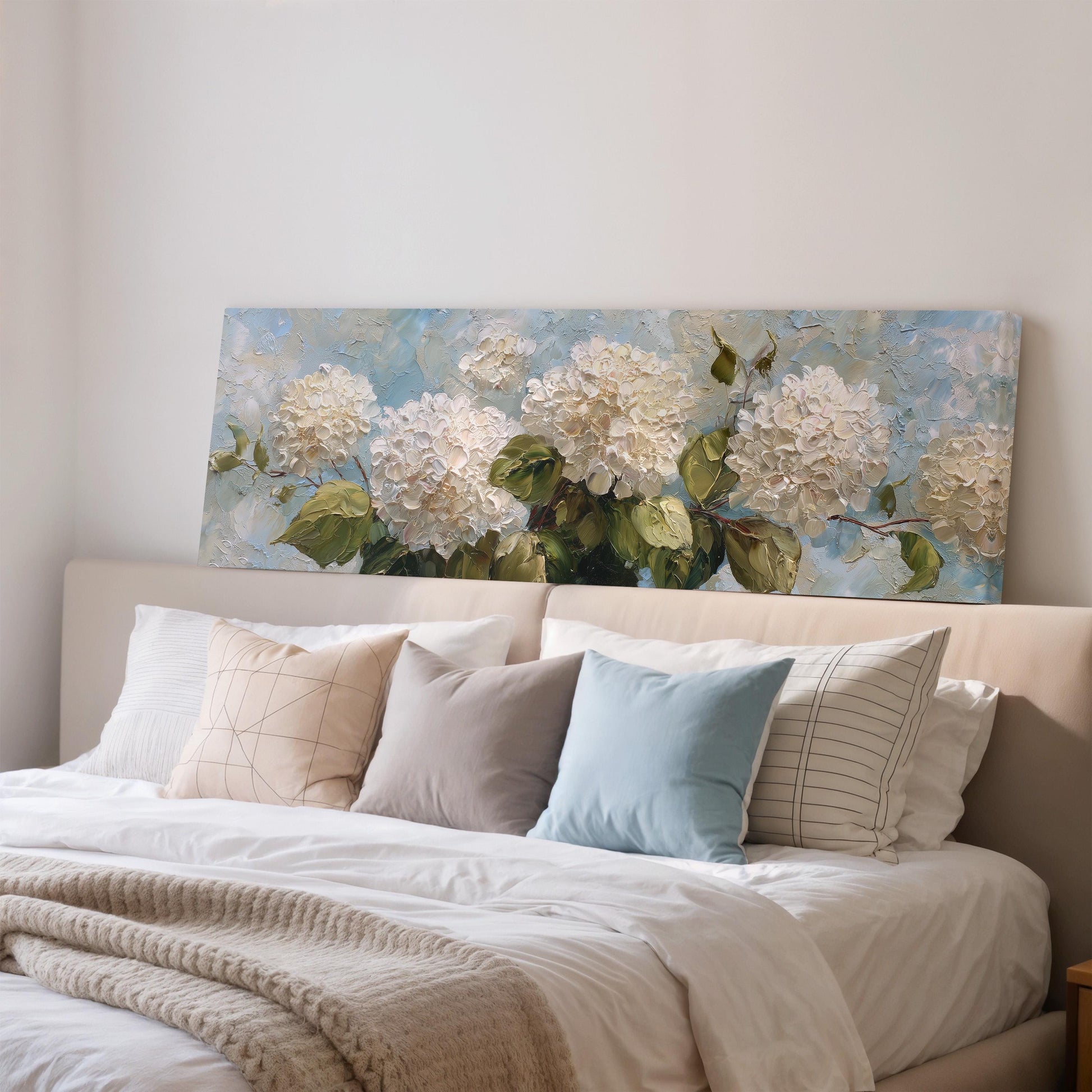 a large painting of white hydrangeas hanging above a bed with white bedding and pillows.
