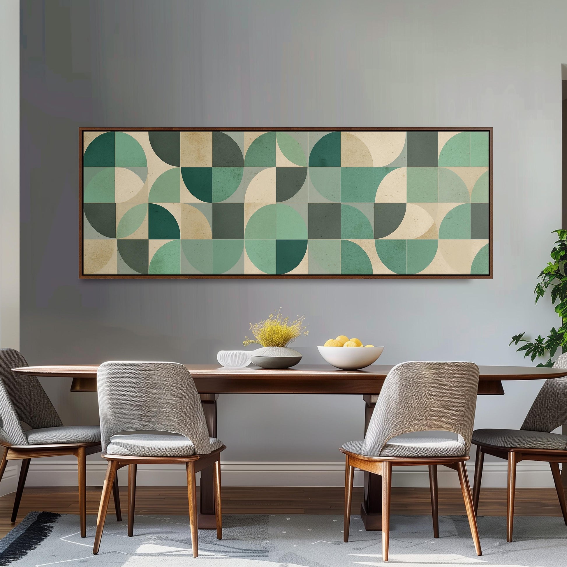 a modern dining room with a wooden table and four gray chairs. Above the table, there is a large abstract painting with a geometric pattern in shades of green and beige. The painting is framed and hangs on the wall above the table.