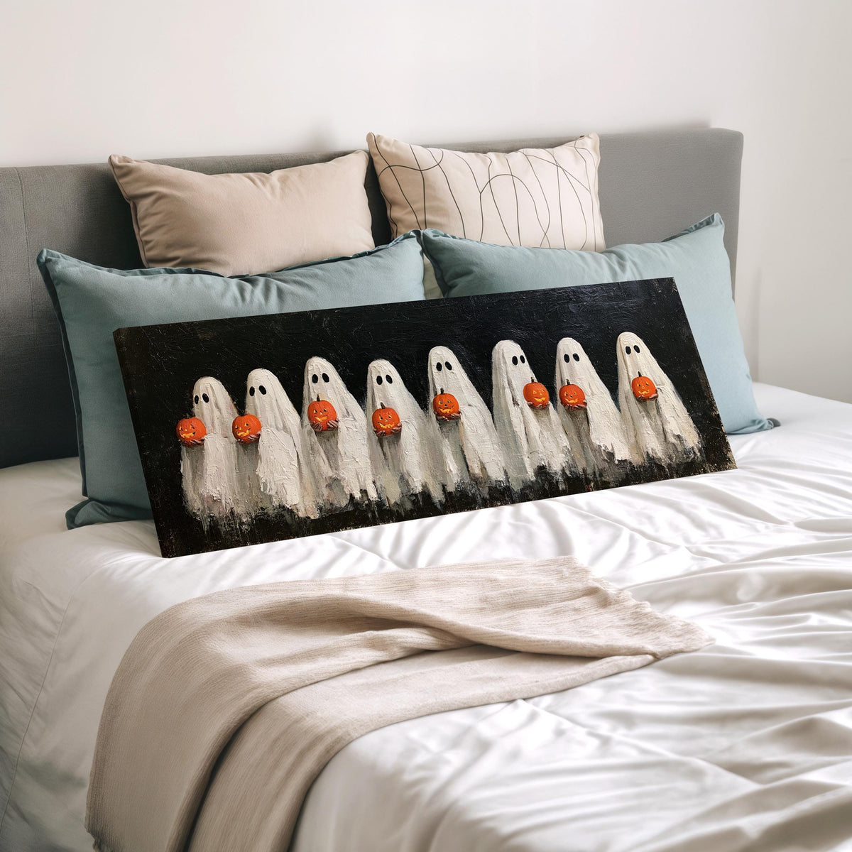 Crowd of huddled ghosts with pumpkins wide panoramic canvas print laid on a bed to show its size