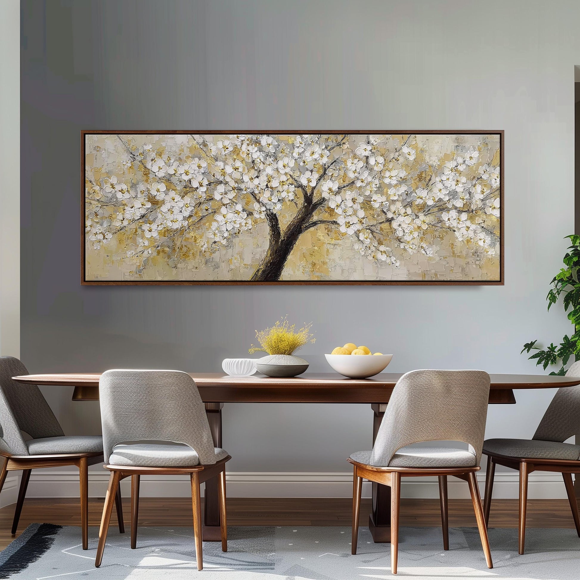 a dining room with a large painting of a tree with white flowers hanging on the wall above a wooden dining table with four chairs. The table is set with a bowl of fruit and a vase of flowers, creating a cozy and inviting atmosphere.