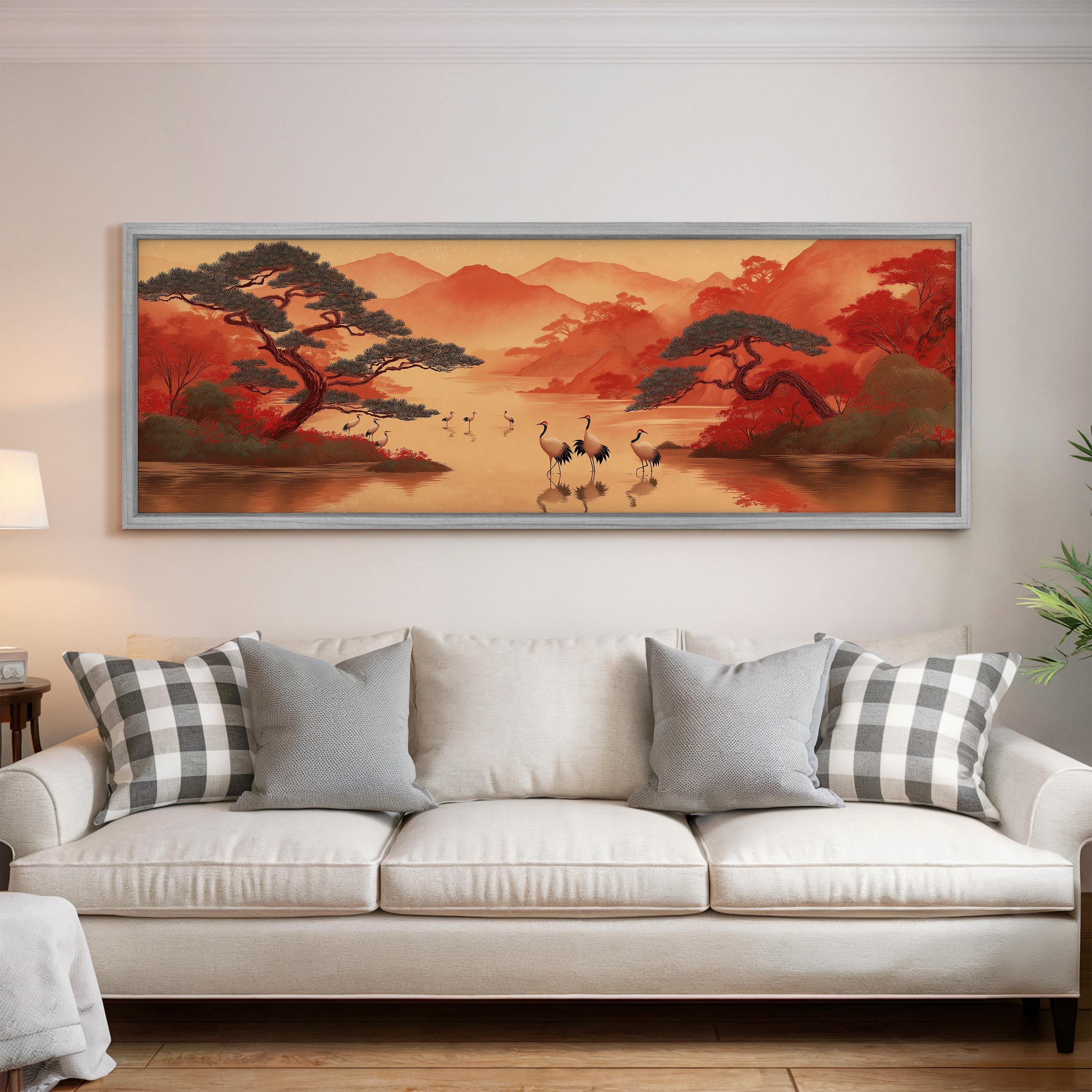 a large, framed painting of a serene landscape with a lake, mountains, and trees, hanging on a wall above a white couch with gray and white patterned pillows.