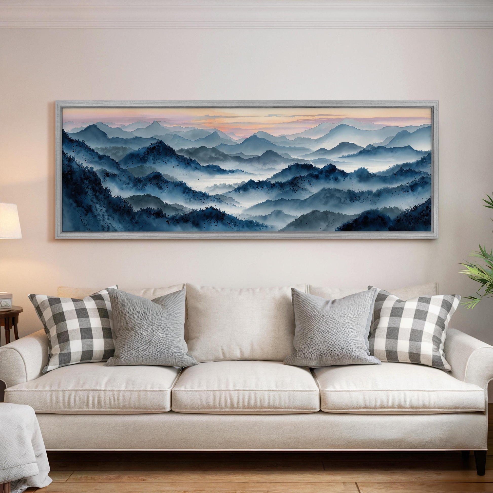 a large, framed painting of a mountainous landscape hanging on a wall above a white couch with gray and white patterned pillows.