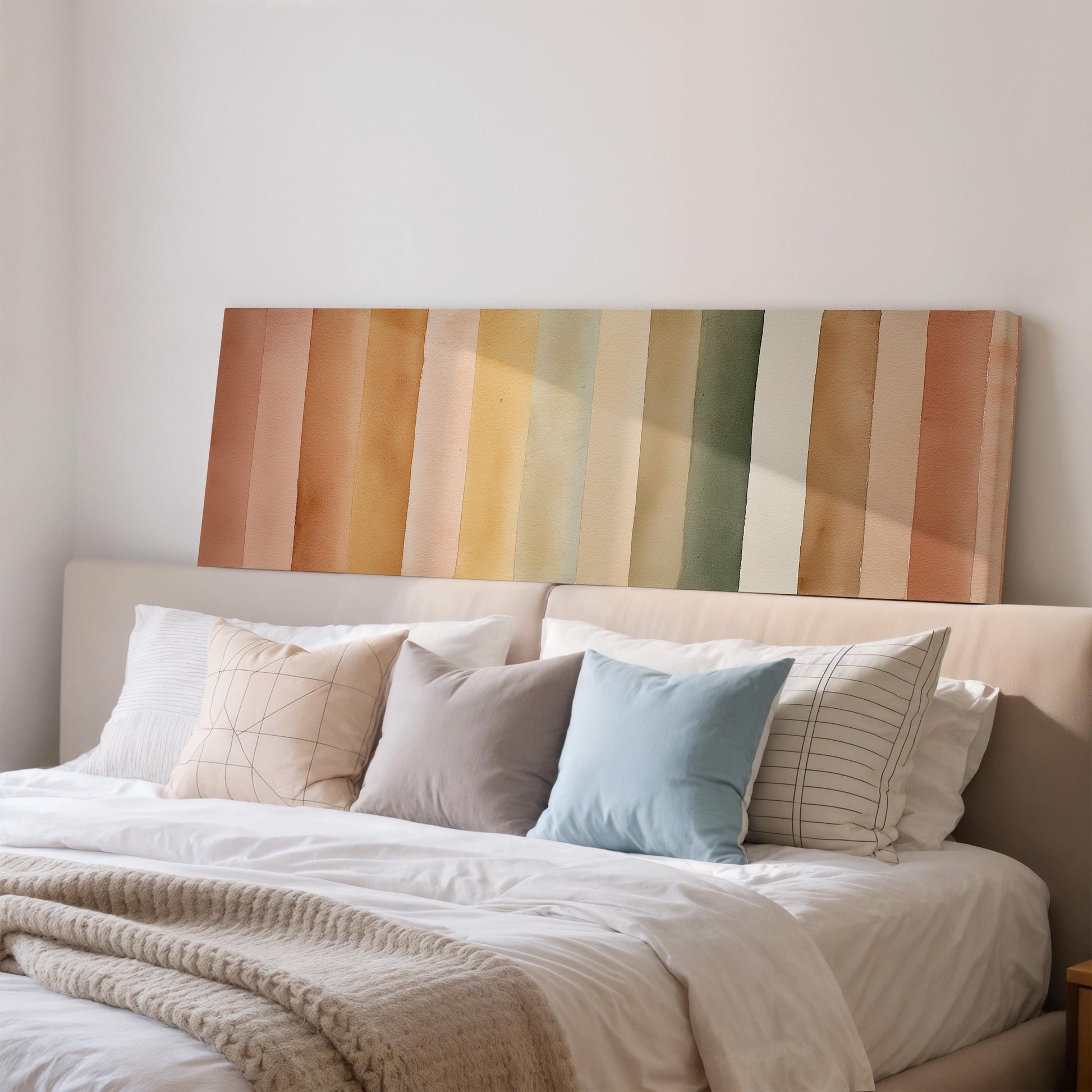 a cozy bedroom with a bed adorned with a variety of colorful pillows. The bed is positioned against a wall, and above it hangs a vibrant, horizontal stripe of warm-toned paint. The overall scene conveys a sense of comfort and warmth, with the bed and its pillows as the focal point.
