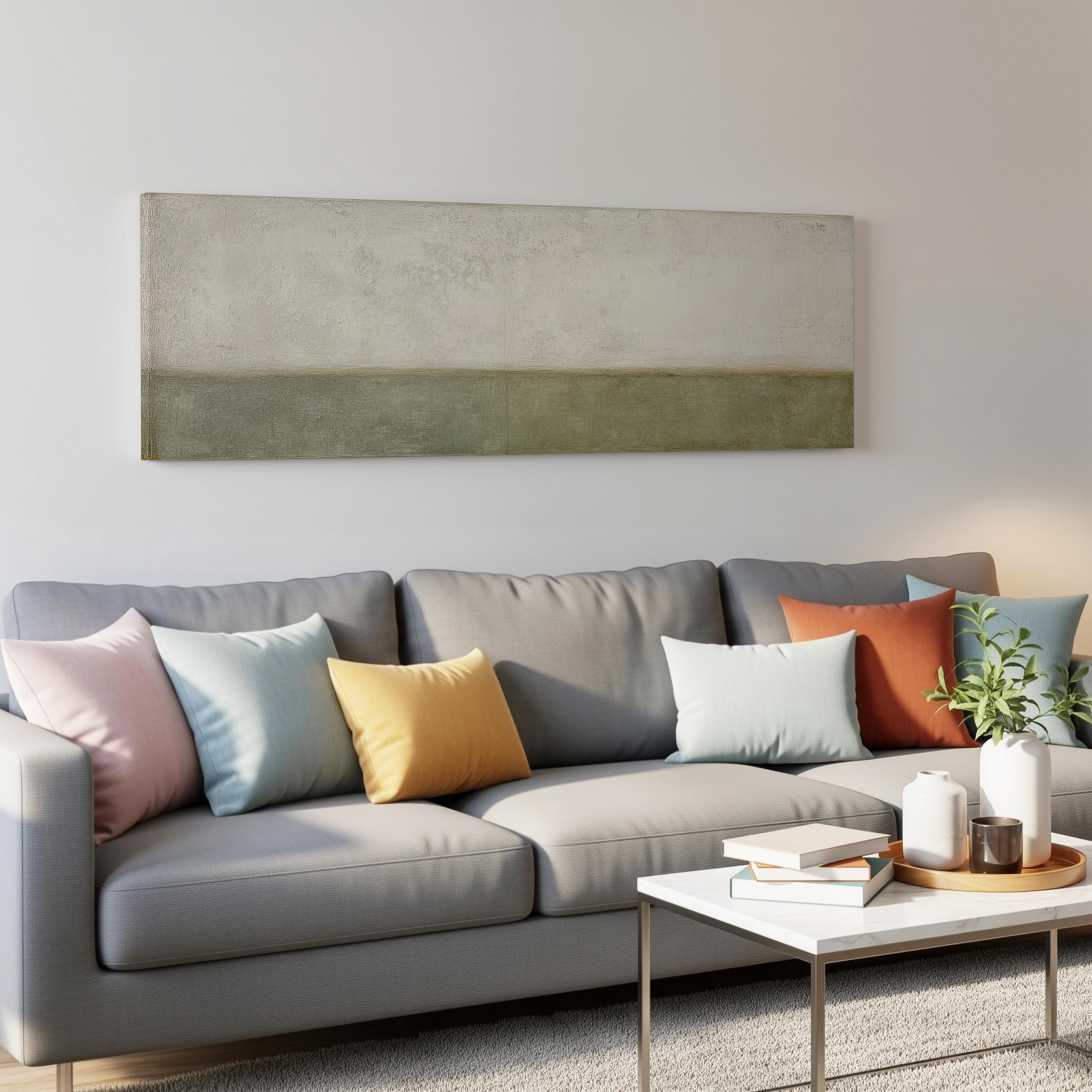 a modern living room with a gray sofa adorned with colorful throw pillows. Above the sofa, there is a large abstract painting on the wall. In front of the sofa, there is a white coffee table with a stack of books and a small plant.