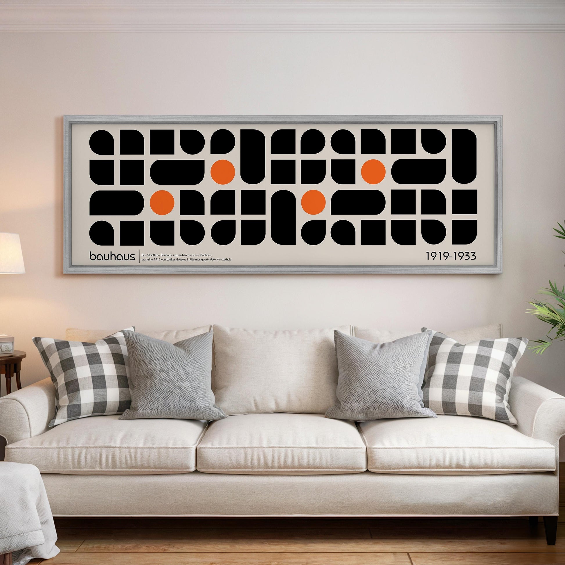 a large framed poster of a geometric design with black and orange shapes, hanging on a wall above a white couch with patterned throw pillows.