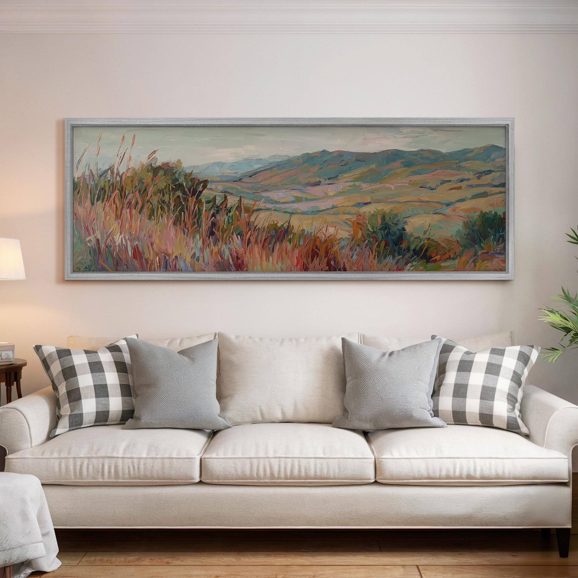 a large, colorful landscape painting hanging on a wall above a white couch with gray and white patterned pillows.