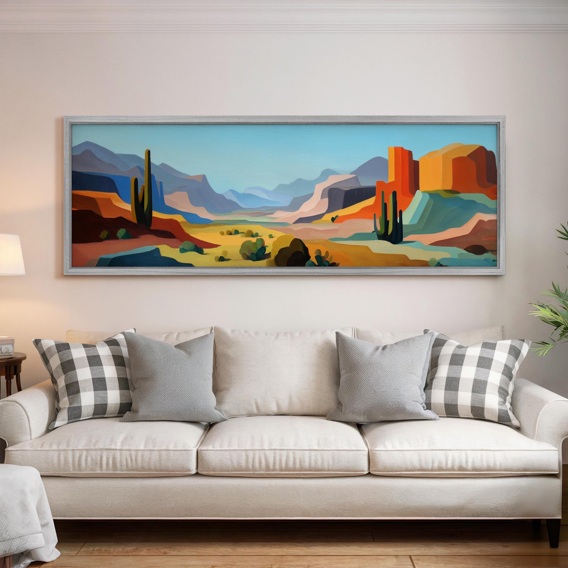 a large, colorful painting of a desert landscape hanging on a wall above a white couch with gray and white plaid throw pillows.