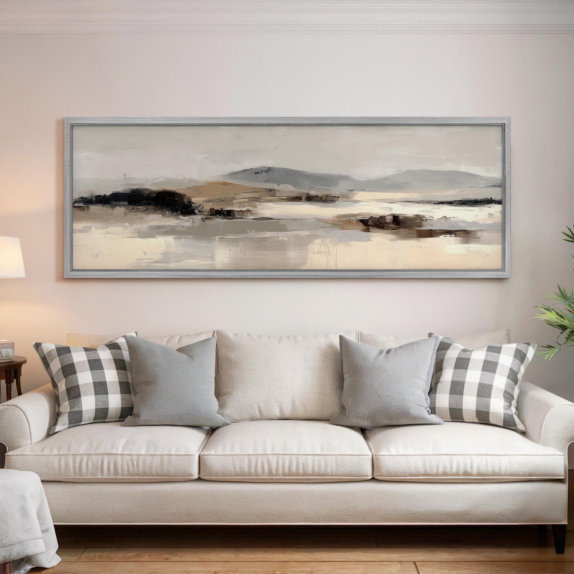 a large, framed landscape painting hanging on a wall above a white sofa with gray and white patterned throw pillows.