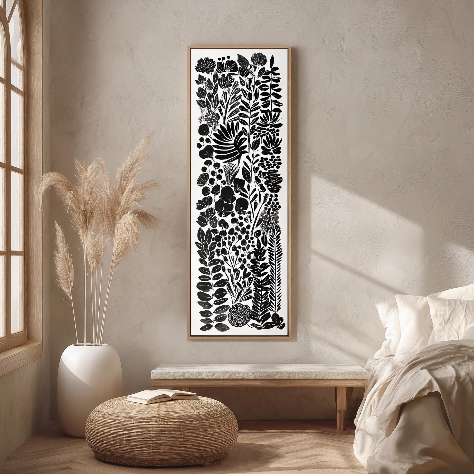 a minimalist bedroom setting with a large black and white abstract artwork hanging on the wall above a wooden bench. The artwork displays a variety of plants and flowers in a vertical arrangement. The room has a neutral color palette, with a white bed, a woven ottoman, and a potted plant adding to the serene and calming atmosphere.