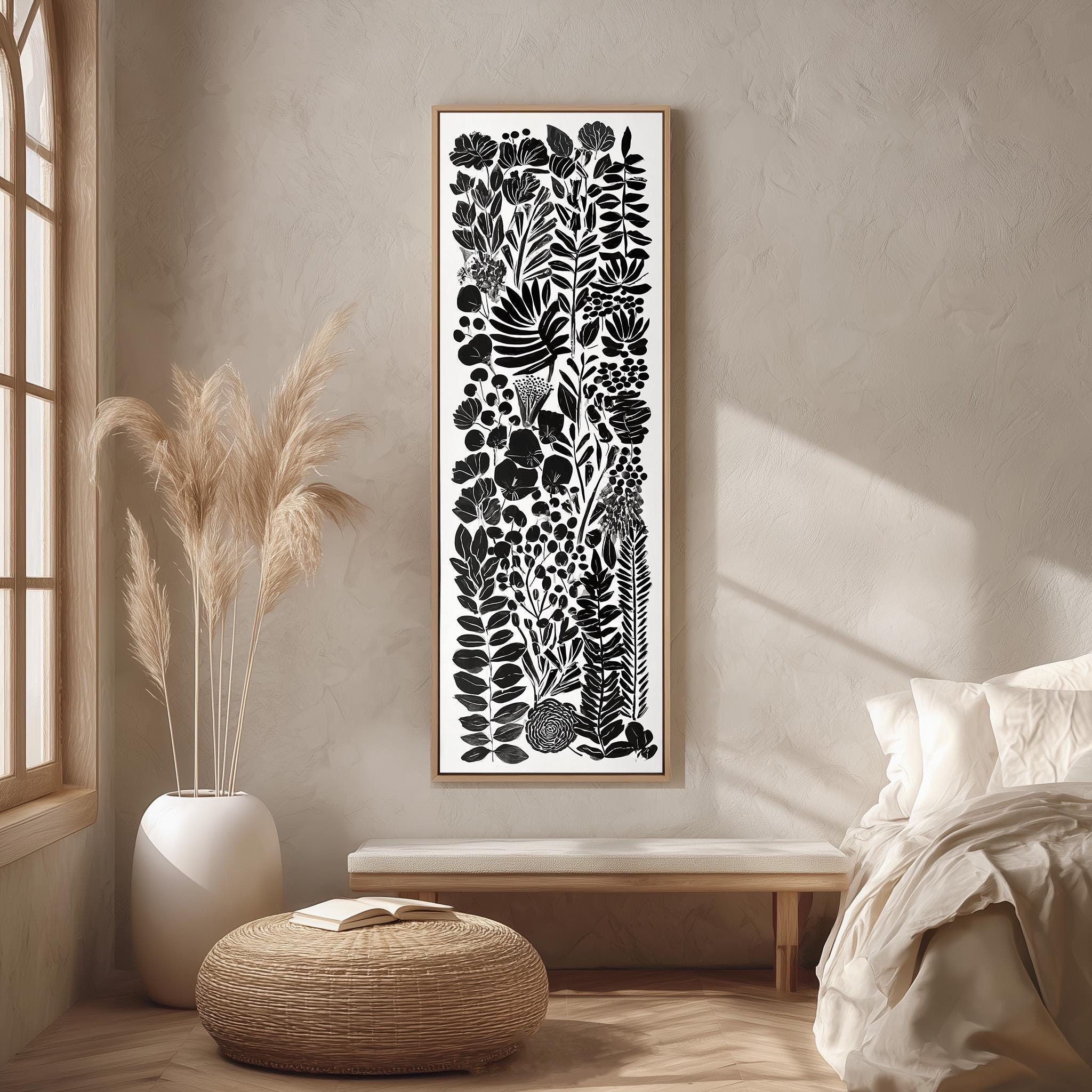 a minimalist bedroom setting with a large black and white abstract artwork hanging on the wall above a wooden bench. The artwork displays a variety of plants and flowers in a vertical arrangement. The room has a neutral color palette, with a white bed, a woven ottoman, and a potted plant adding to the serene and calming atmosphere.