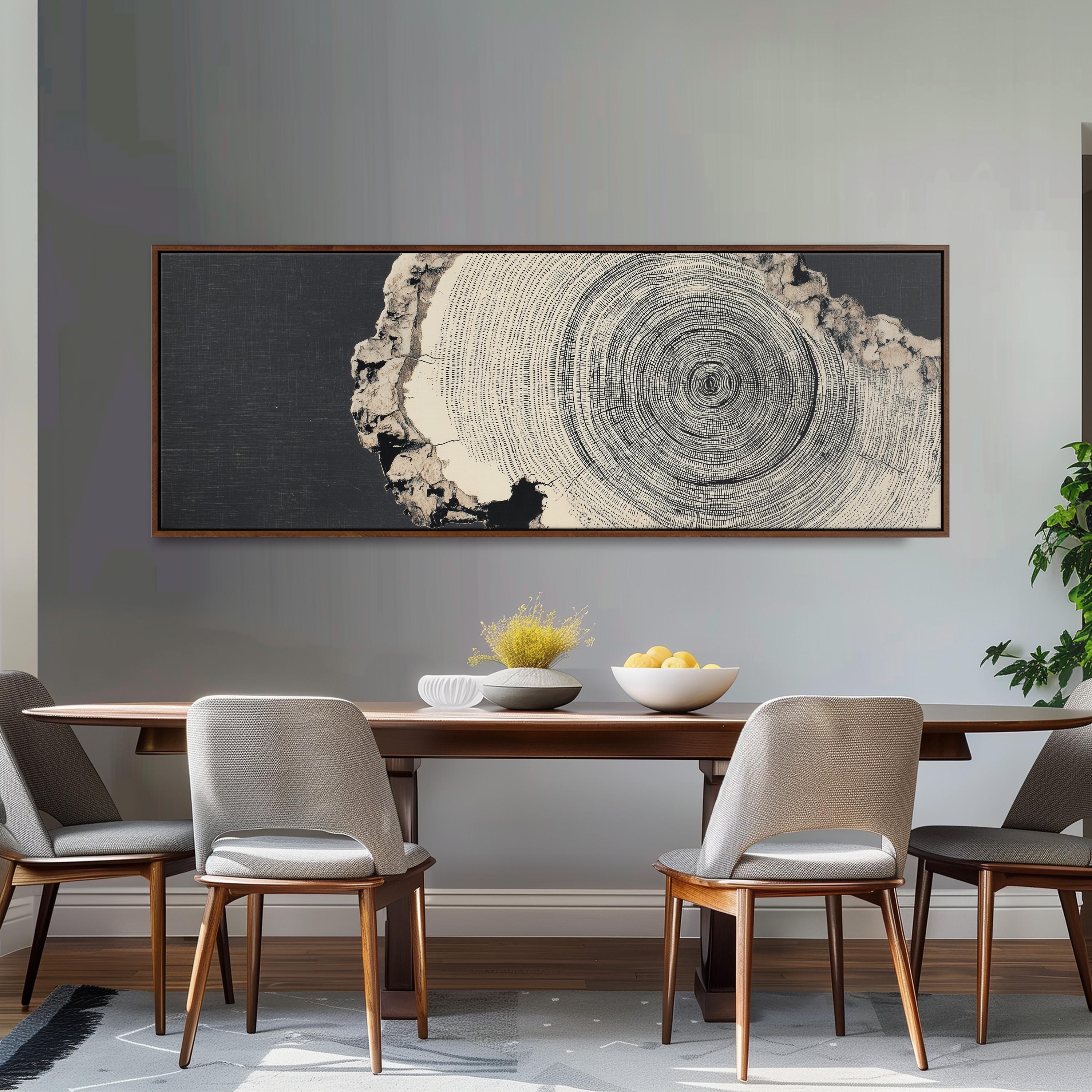 a dining room with a wooden table and four chairs. Above the table, there is a large black and white tree trunk painting hanging on the wall. On the table, there is a bowl of fruit and a vase of flowers.